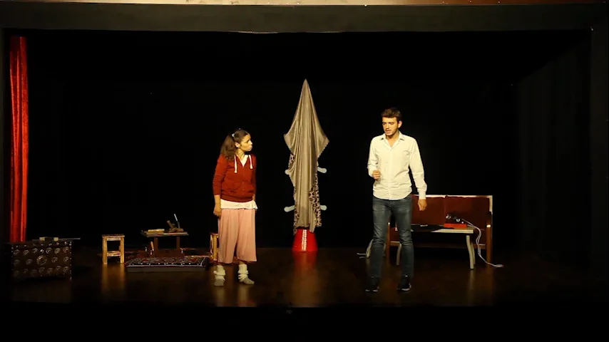 sahnede iki oyuncu, arkada uçma aletini temsil eden dekor